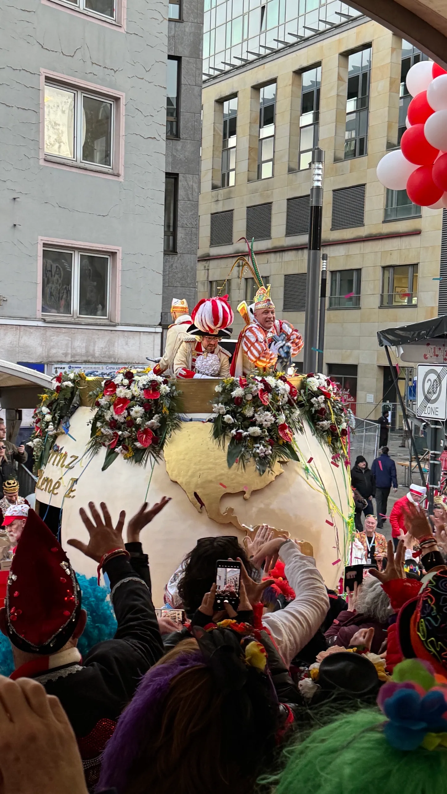 Der Prinzenwagen des Rosenmontagszugs 2026 mit Blumenschmuck, davor winkende Hände auf der Tribüne