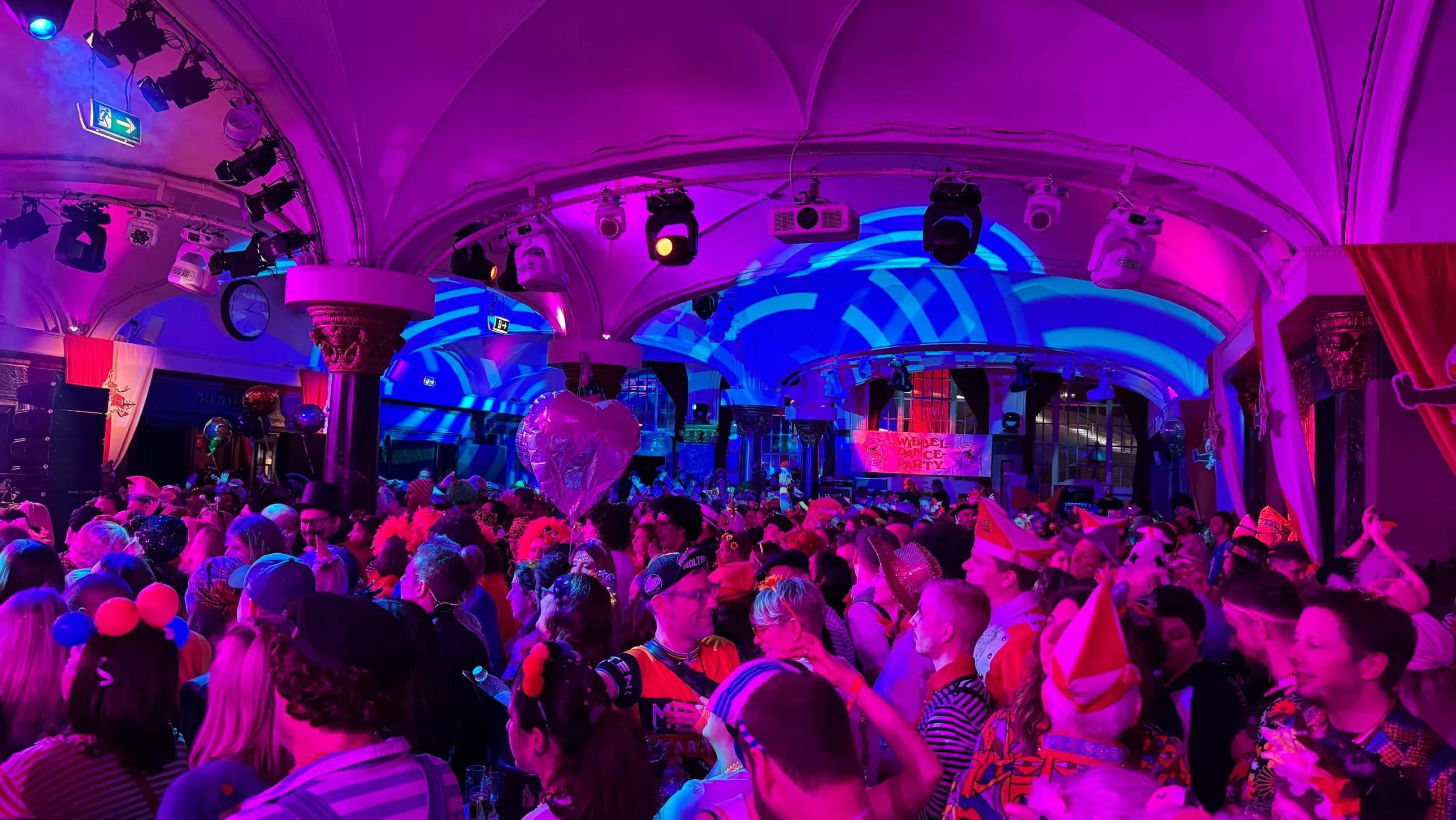 Voller Wartesaal am Dom im violetten Licht, Wibbeldance-Party-Banner über der Bühne